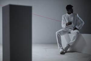 A picture of a person sitting opposite a block in a room connected by a red wire to a device in their hand. The red wire signifies the increasing trend of using mesh networking solutions and mesh Wi-Fi systems to extend network coverage, connect with more devices, and manage office networks seamlessly.
